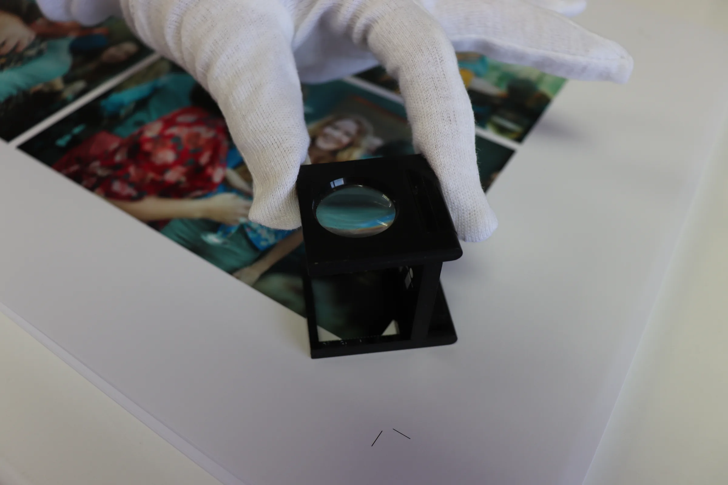A gloved hand inspecting a photographic print with a linen tester