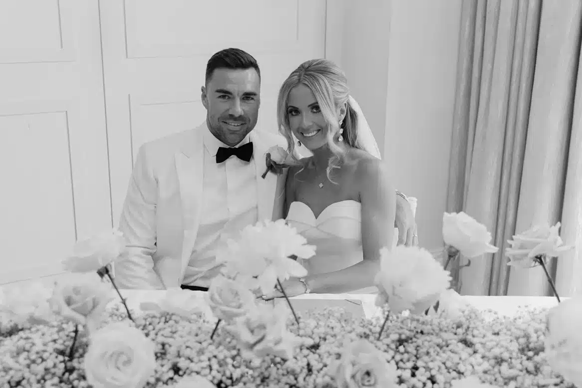 Newly married couple seated behind flowers at their wedding reception