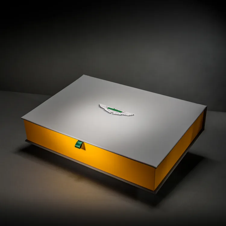Closed silver Aston Martin presentation box with a golden edge and green ribbon pull