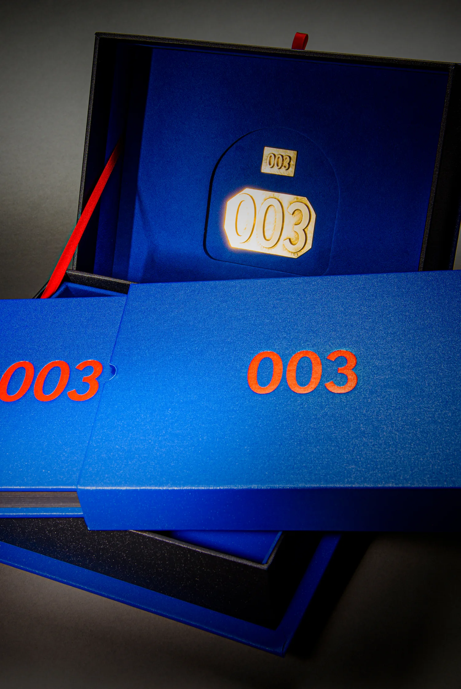 Blue numbered 003 book and matching presentation case with red ribbons and an illuminated gold number