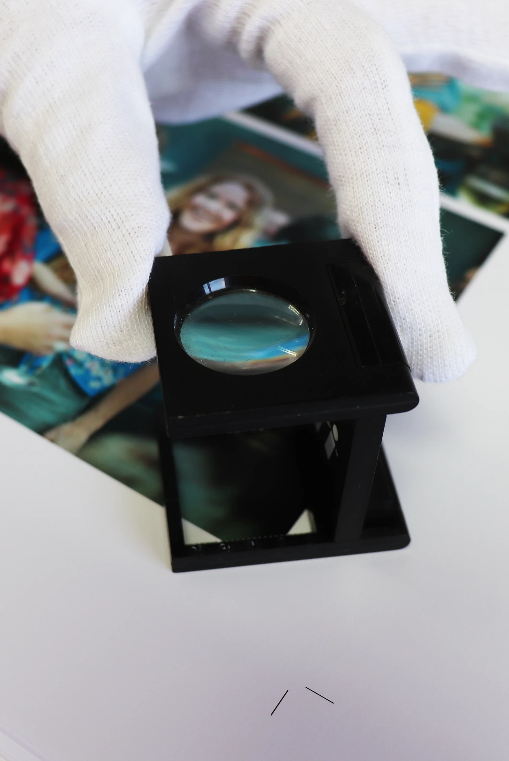 Gloved hands inspecting a photographic print through a linen tester