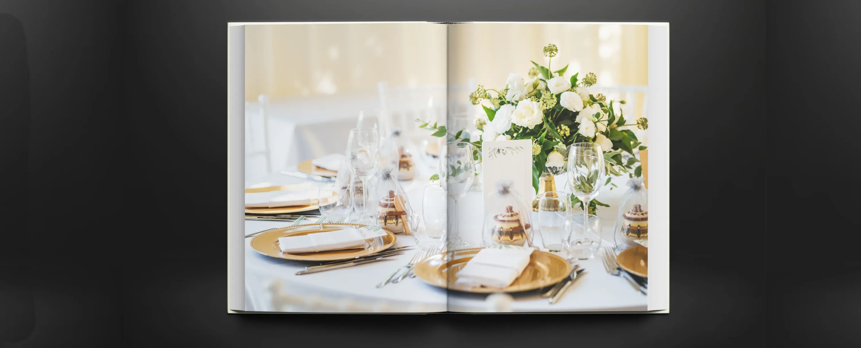 Open wedding photo book displaying an elegant reception table with white flowers and gold place settings