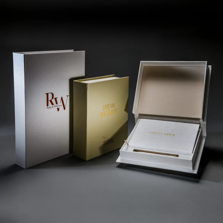 Three personalised wedding books and presentation boxes arranged on a dark studio backdrop