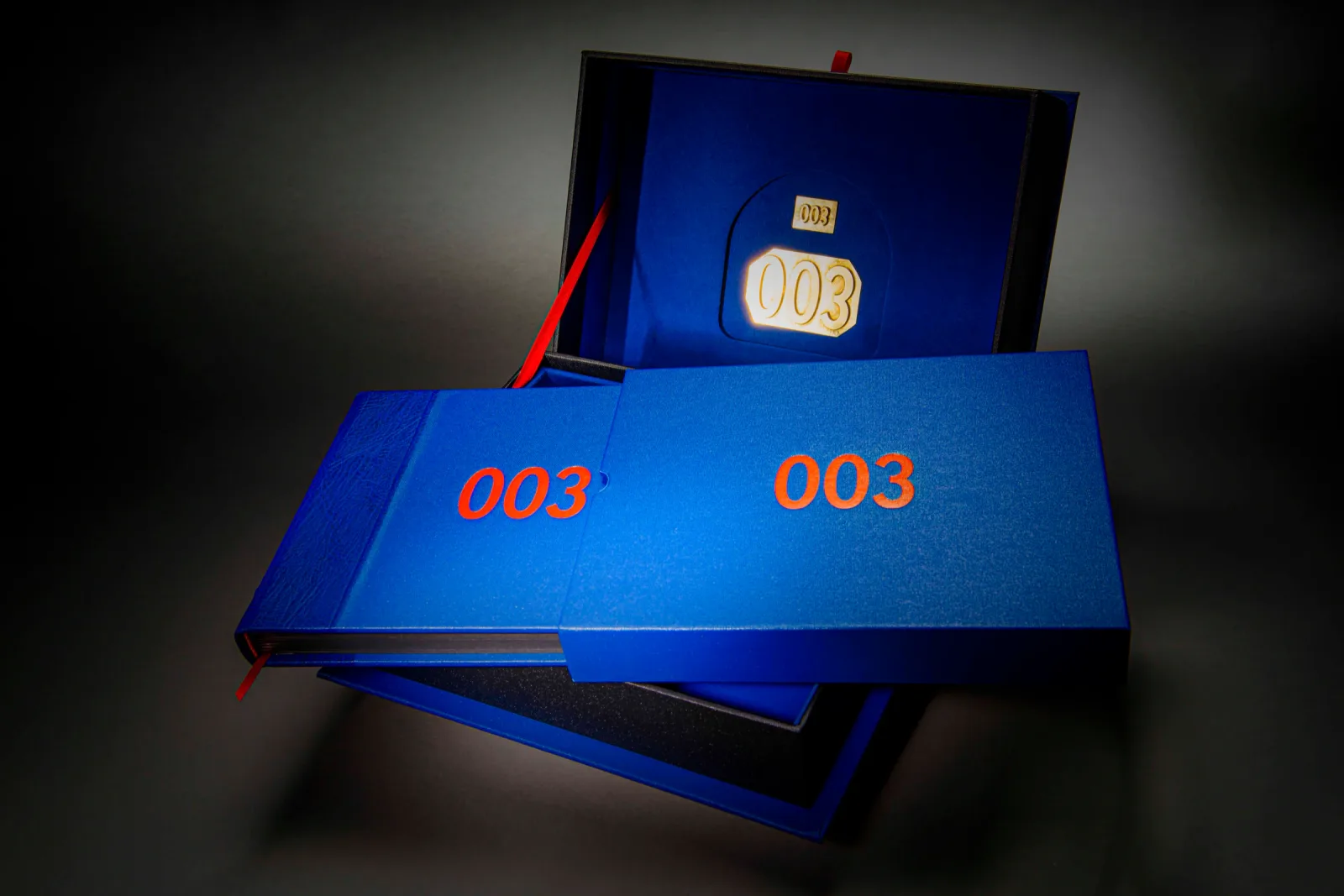 Blue photo book and matching presentation box with orange 003 titles and red ribbon markers