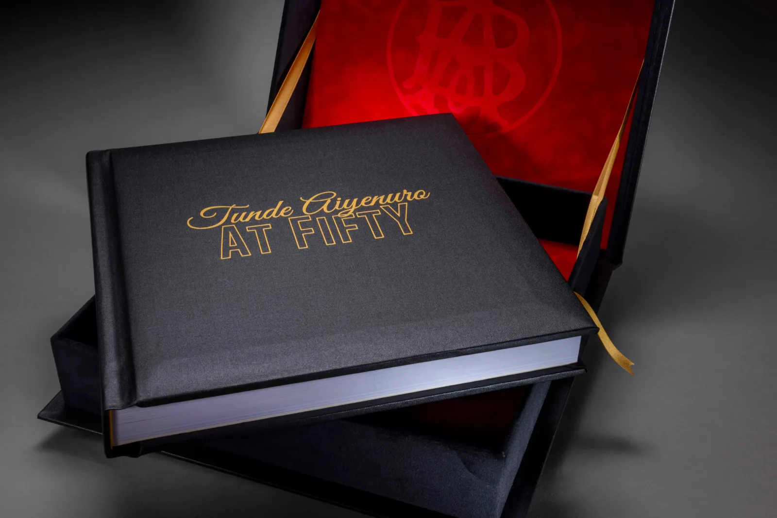 Black cloth photo book with a gold-foiled fiftieth-birthday title beside a red-lined presentation box
