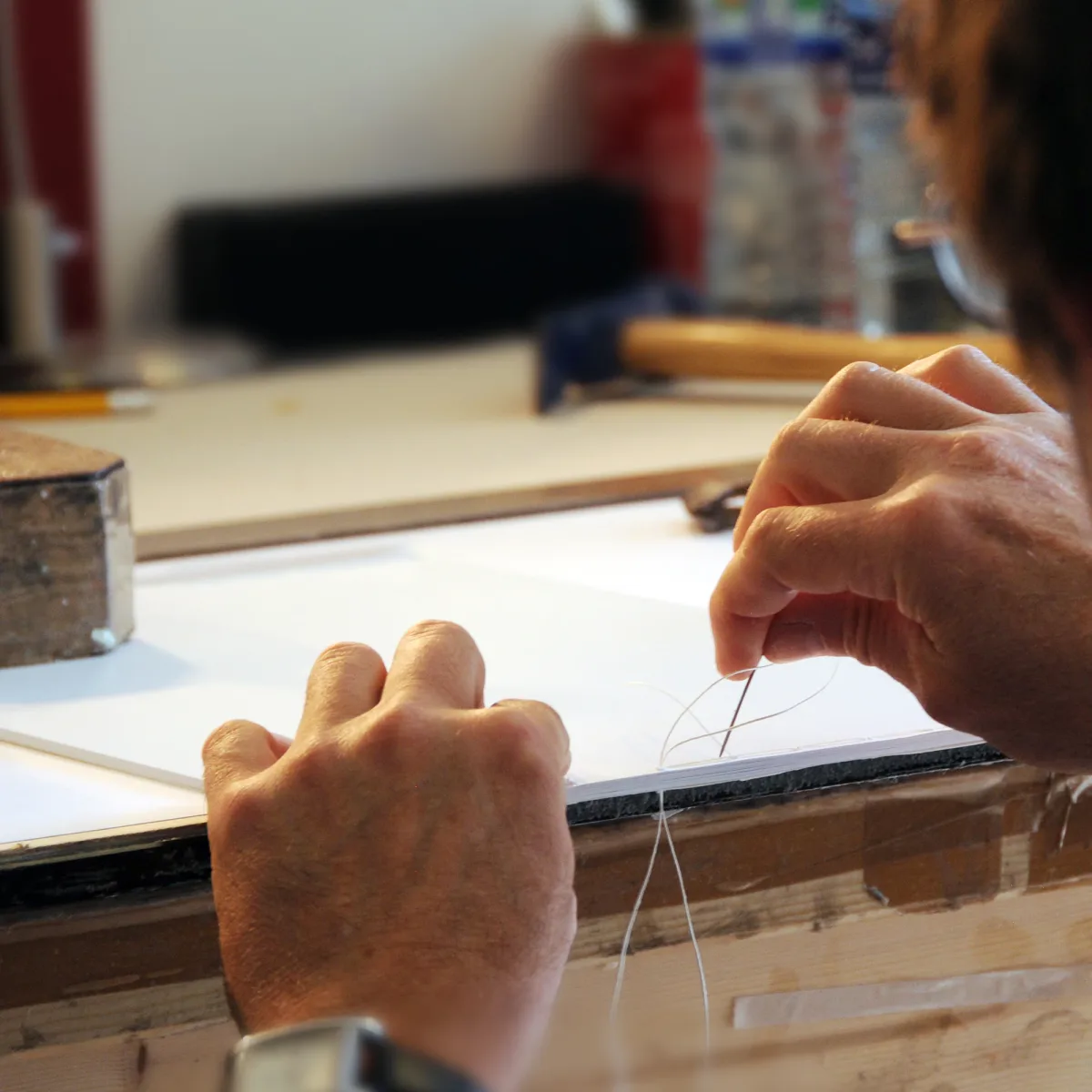Close-up of a bookbinder hand stitching a photo book with a needle and white thread