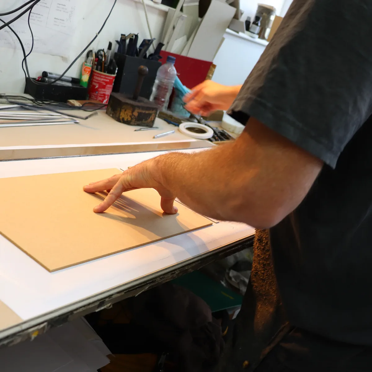 Bookbinder aligning a cover board with a straightedge on a workshop bench